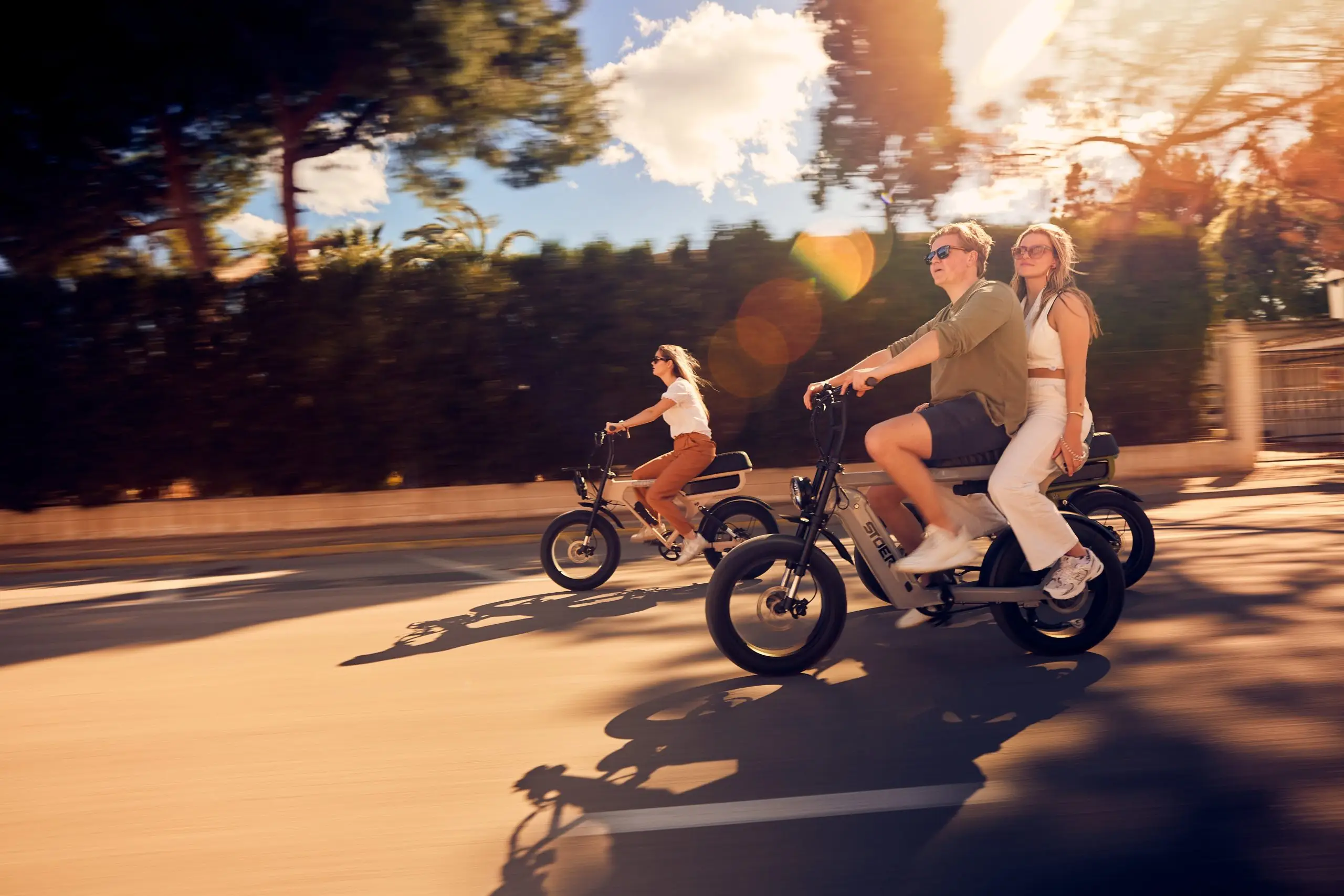 Drei Personen fahren bei Sonnenschein auf STOER E-Fatbikes durch eine Straße, zwei davon gemeinsam auf einem Bike